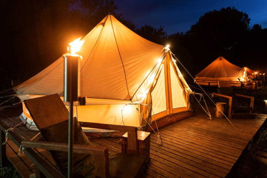 Tents with burning torches, lamps and wooden chairs at glamping, forest around, night